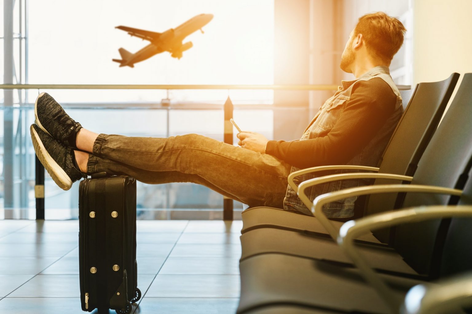 Conheça as exigências para a entrada de brasileiros que viajam para o exterior man sitting on gang chair with feet on luggage looking at airplane